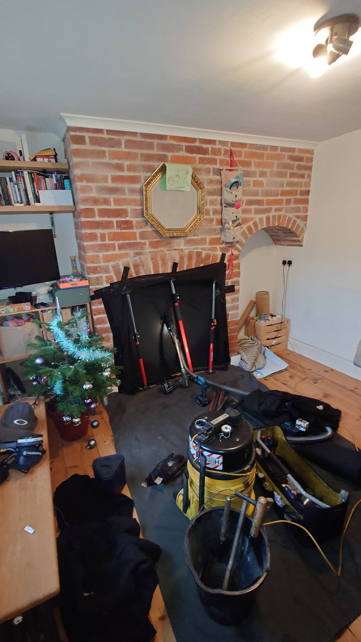 Sweeping kit set up at a brick inglenook: dust sheet, vacuum and rods, with a Christmas tree in the corner
