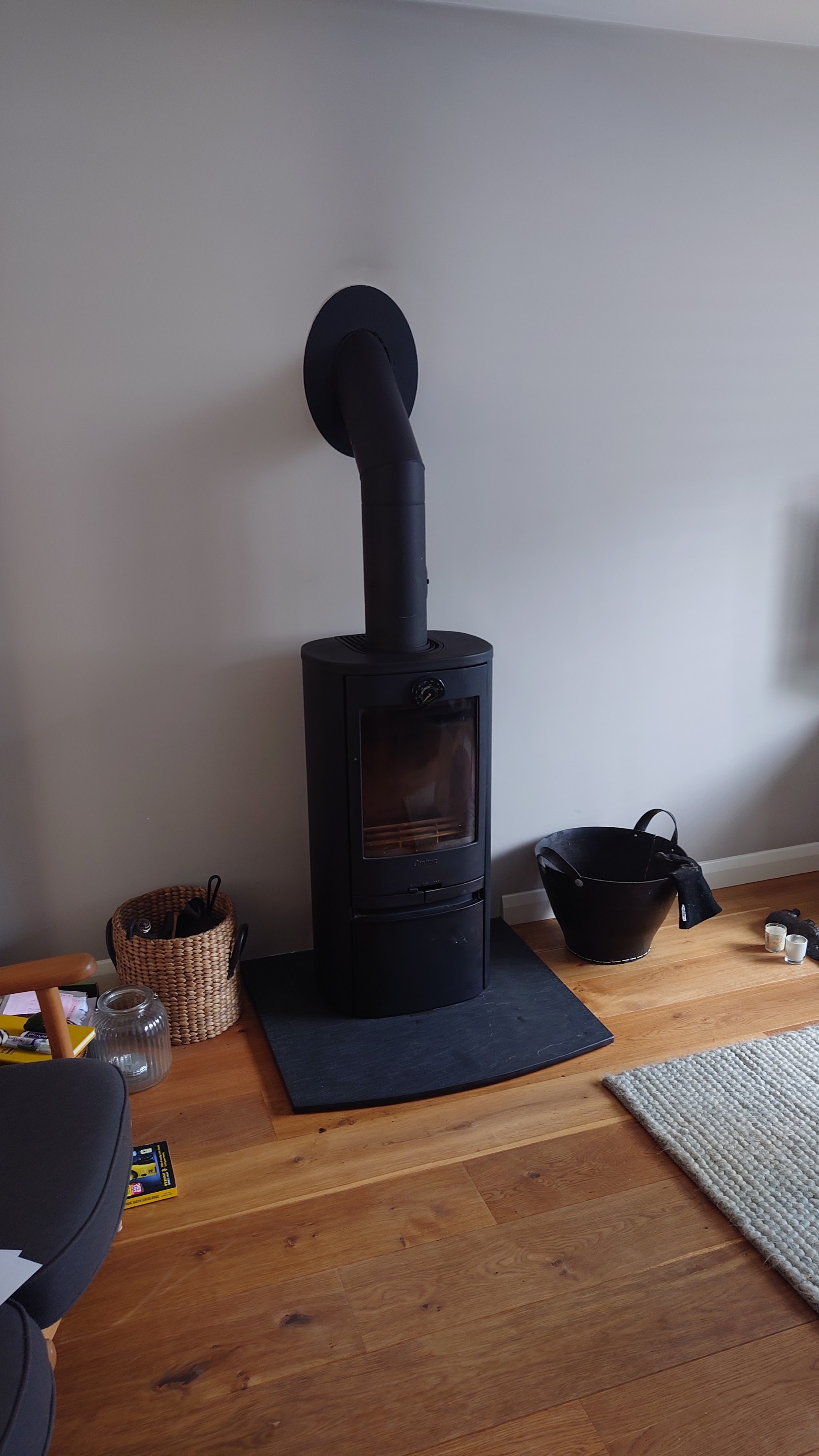 Black freestanding wood stove with its flue on a slate hearth, oak floor and kindling basket