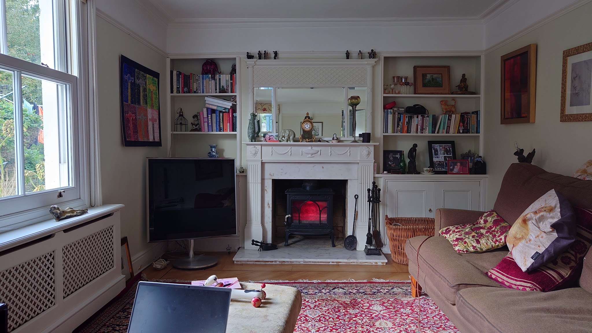 Victorian sitting room with a white mantel, a lit stove and bookshelves either side