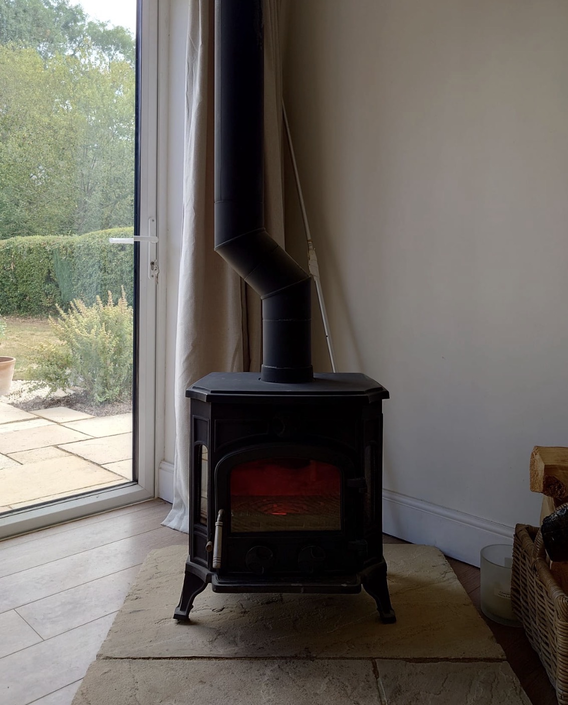 Black stove and flue lit beside patio doors on a stone hearth